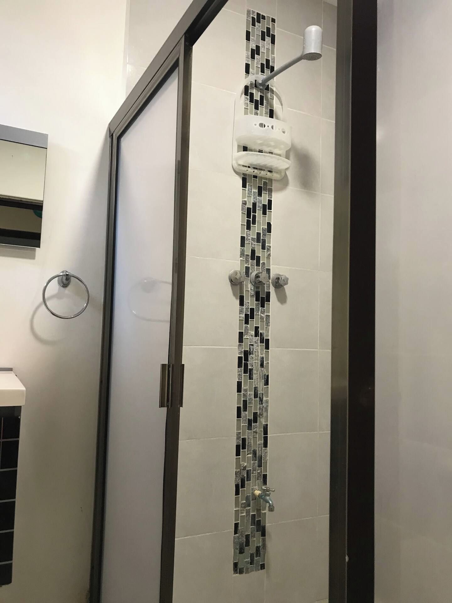 Une douche avec une porte en verre, un mur blanc orné de motifs en mosaïque et un porte-serviette fixé au mur.