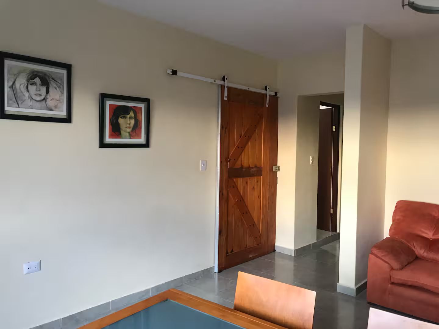 A hallway with a wooden door, a framed picture, and a red sofa.