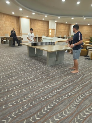 Una habitación con mesa de ping pong, alfombra estampada y pared de ladrillo.