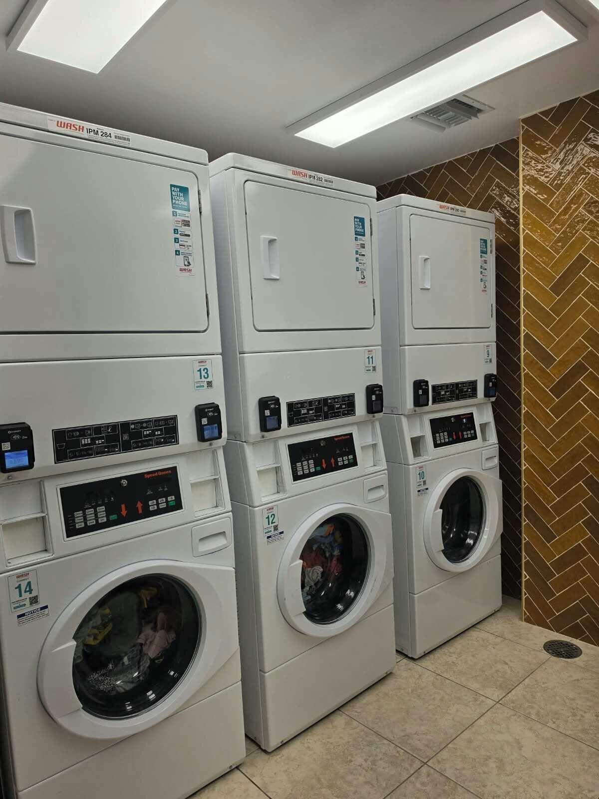 A row of stacked front-loading washing machines in a commercial setting.