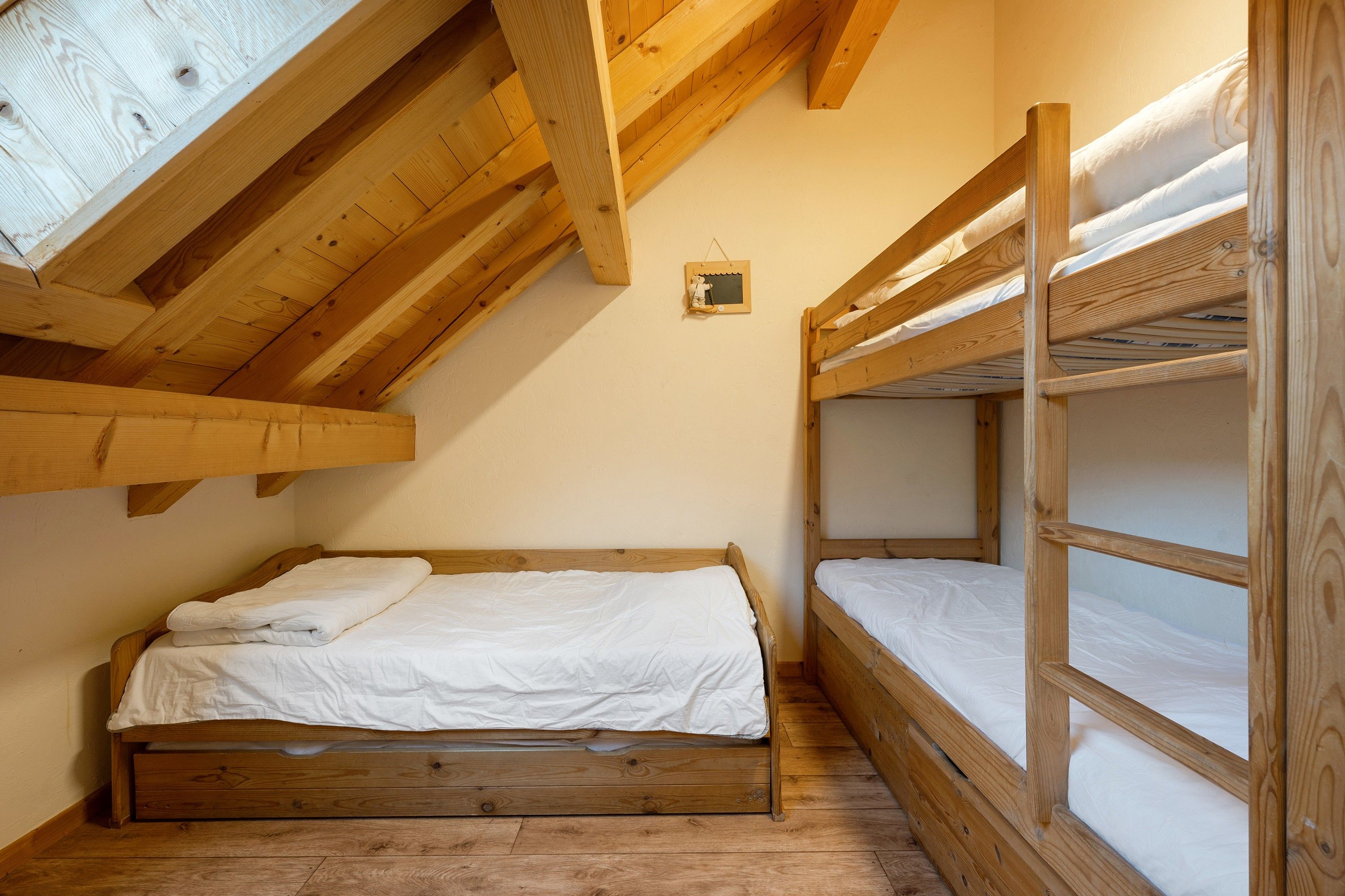A room with a sloped ceiling, wooden bunk beds, and a small wall-mounted shelf.