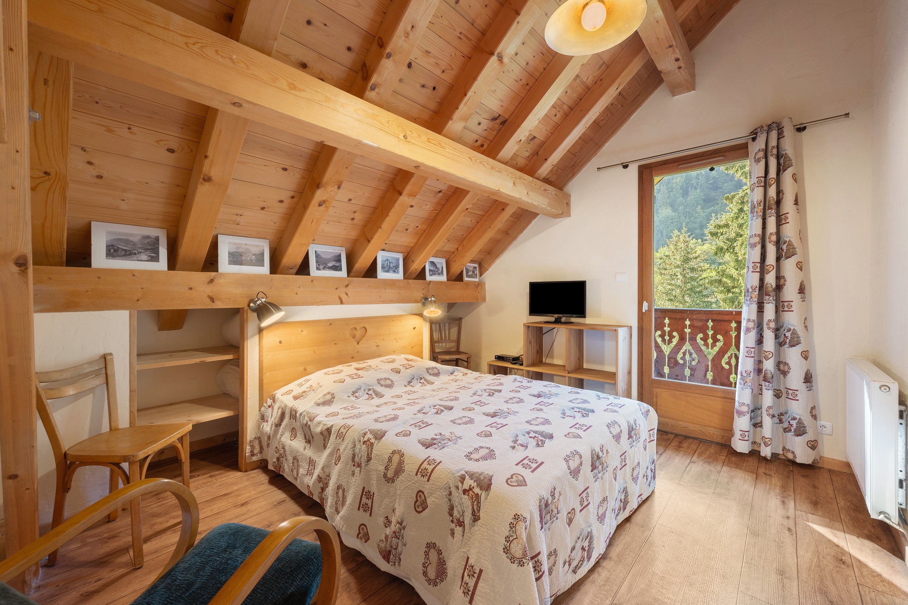 Une pièce chaleureuse avec un plafond en bois, un lit recouvert d’une courtepointe à motifs, un bureau avec un ordinateur et une fenêtre avec des rideaux.