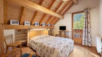 Um quarto aconchegante com teto de madeira, uma cama com colcha estampada, uma escrivaninha com computador e uma janela com cortinas.