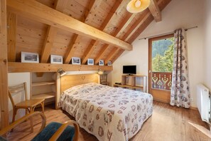 A cozy room with a wooden ceiling, a bed with a patterned bedspread, a desk with a computer, and a window with curtains.