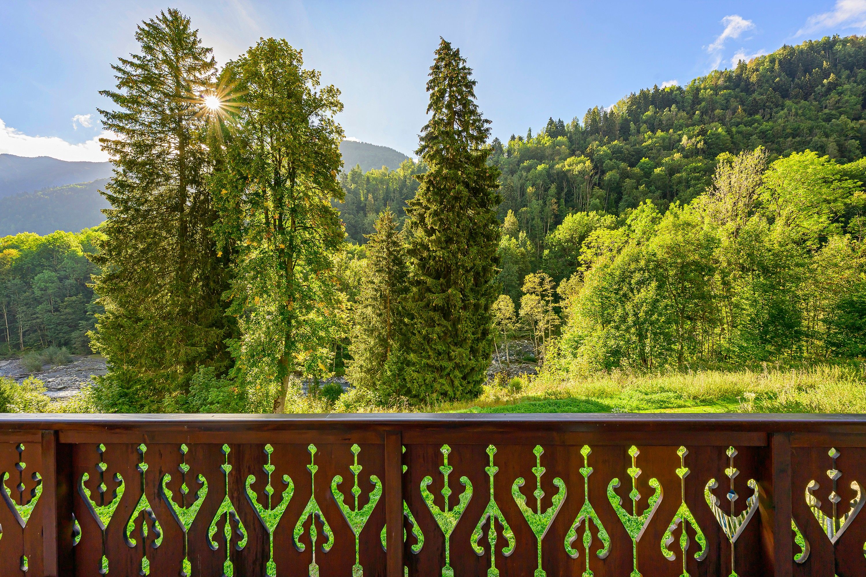 A scenic view of a forested mountain area with a wooden fence in the foreground.