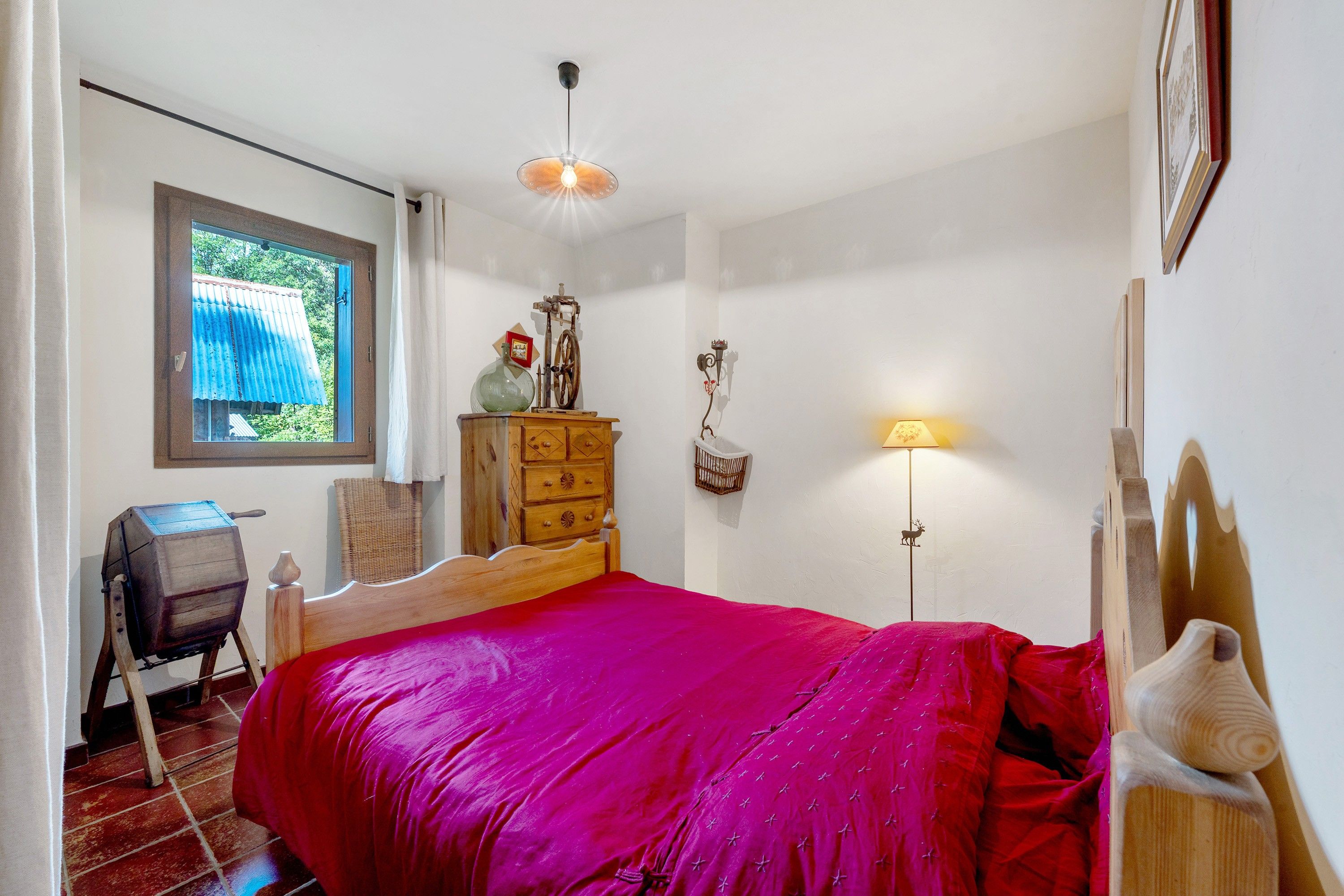 A bedroom with a wooden bed, a dresser, a desk, a window with curtains, and a wall-mounted lamp.