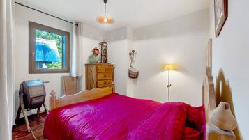 A bedroom with a wooden bed, a dresser, a desk, a window with curtains, and a wall-mounted lamp.