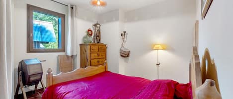 A bedroom with a wooden bed, a dresser, a desk, a window with curtains, and a wall-mounted lamp.