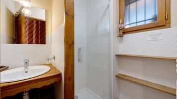 A bathroom with a wooden vanity, a mirror, a shower enclosure, and a small window.