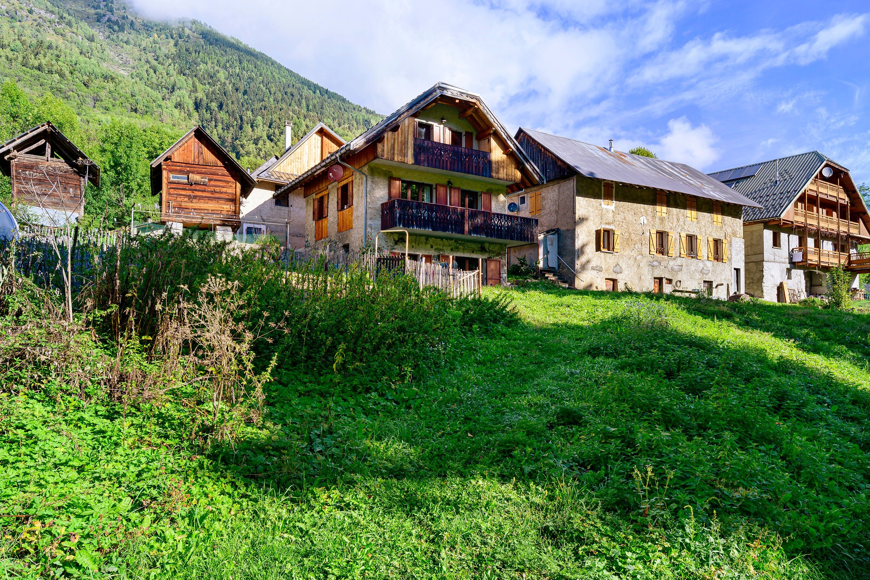A traditional chalet-style building with multiple balconies and a sloped roof, surrounded by lush greenery and a mountainous backdrop.