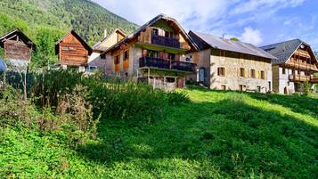 A traditional chalet-style building with multiple balconies and a sloped roof, surrounded by lush greenery and a mountainous backdrop.