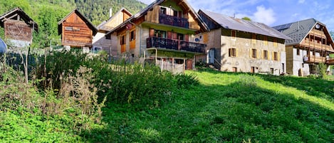 A traditional chalet-style building with multiple balconies and a sloped roof, surrounded by lush greenery and a mountainous backdrop.