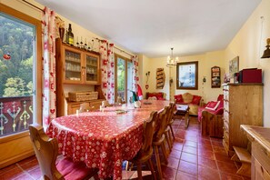 A dining area with a red tablecloth, wooden chairs, a cabinet with glass doors, and a view of greenery outside.