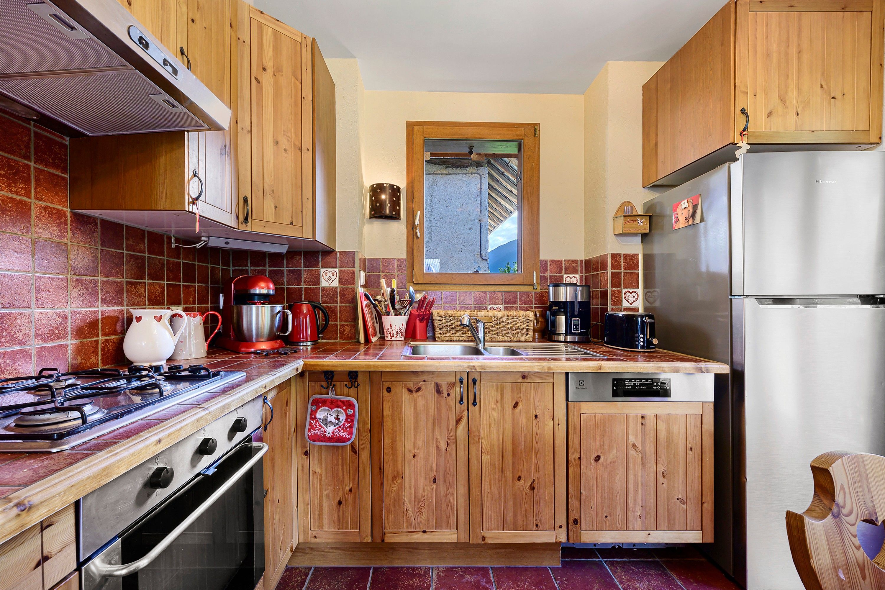 Une cuisine avec des meubles de rangement en bois, un réfrigérateur en acier inoxydable, une cuisinière et une fenêtre au-dessus de l’évier.