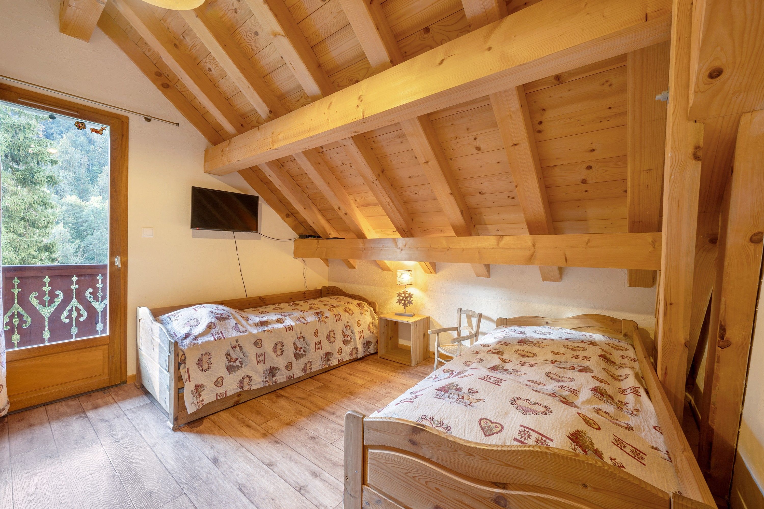 A room with two wooden bunk beds, a television mounted on the wall, and a window with a view of trees.