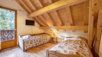 A room with two wooden bunk beds, a television mounted on the wall, and a window with a view of trees.