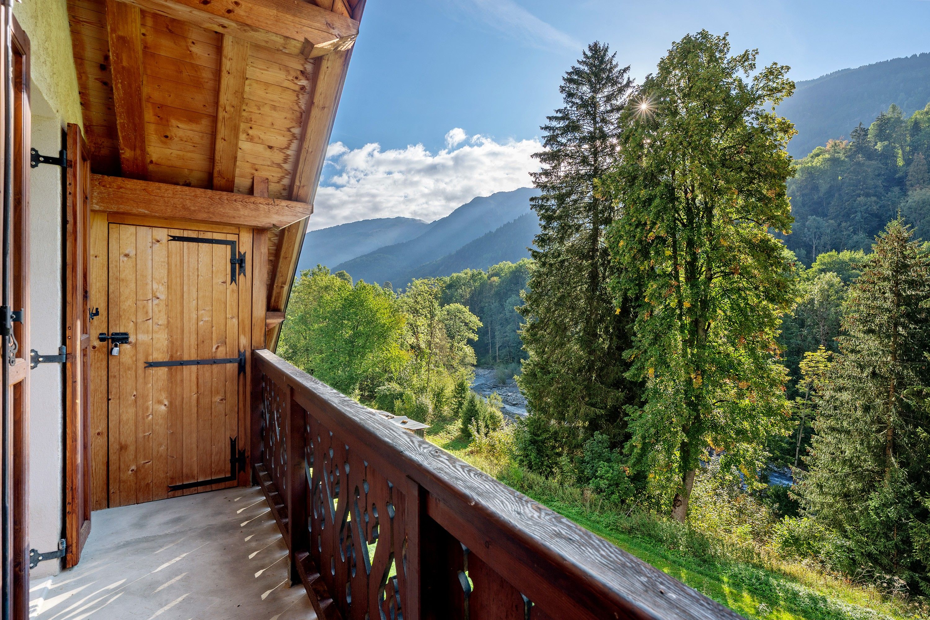 Un balcon en bois offrant une vue sur une forêt et des montagnes.