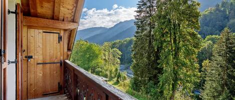 A wooden balcony with a view of a forest and mountains.