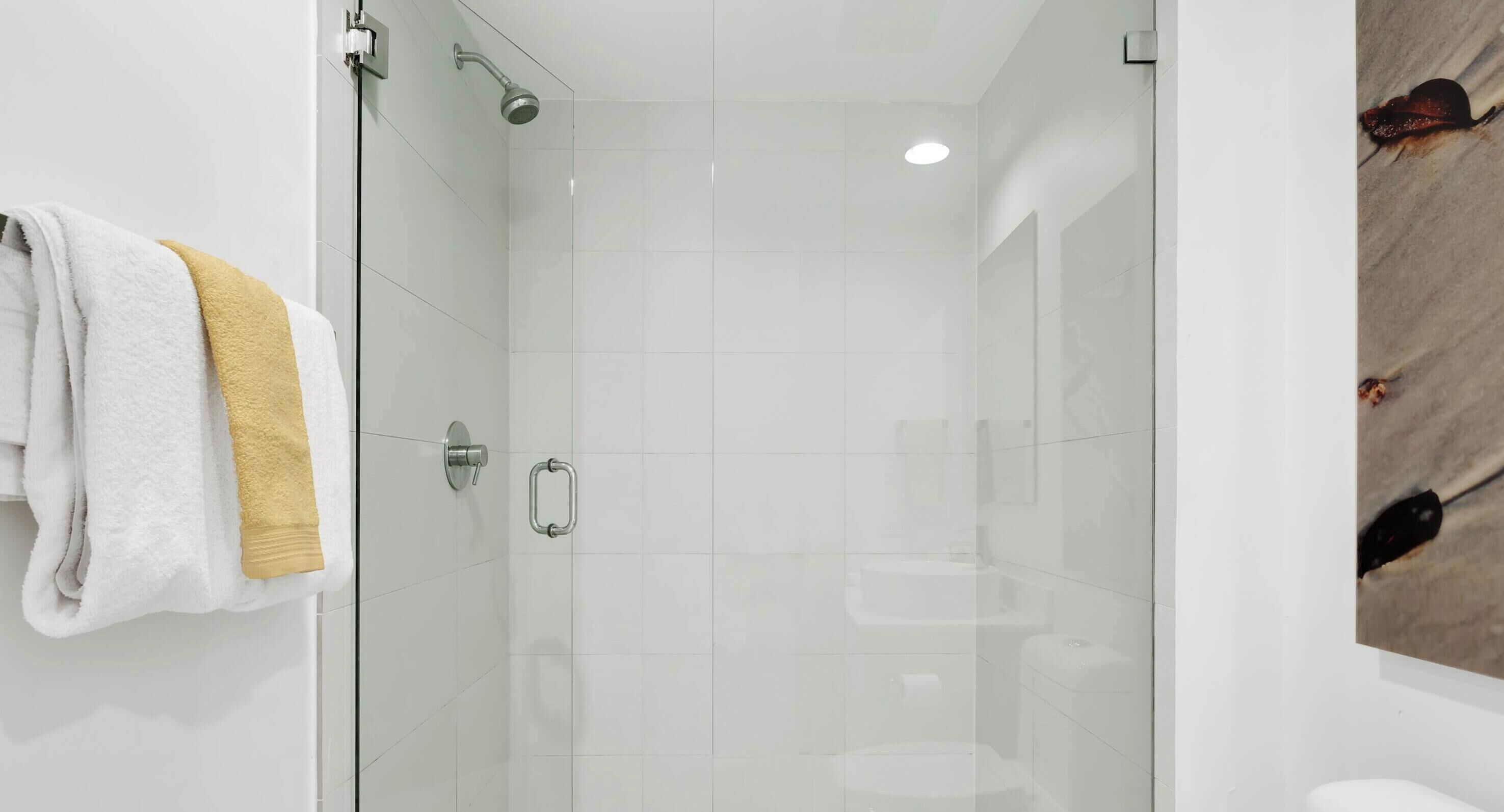 Une salle de bain moderne avec une douche à parois de verre, un porte-serviettes avec des serviettes blanches et jaunes, et des toilettes visibles à travers le verre.
