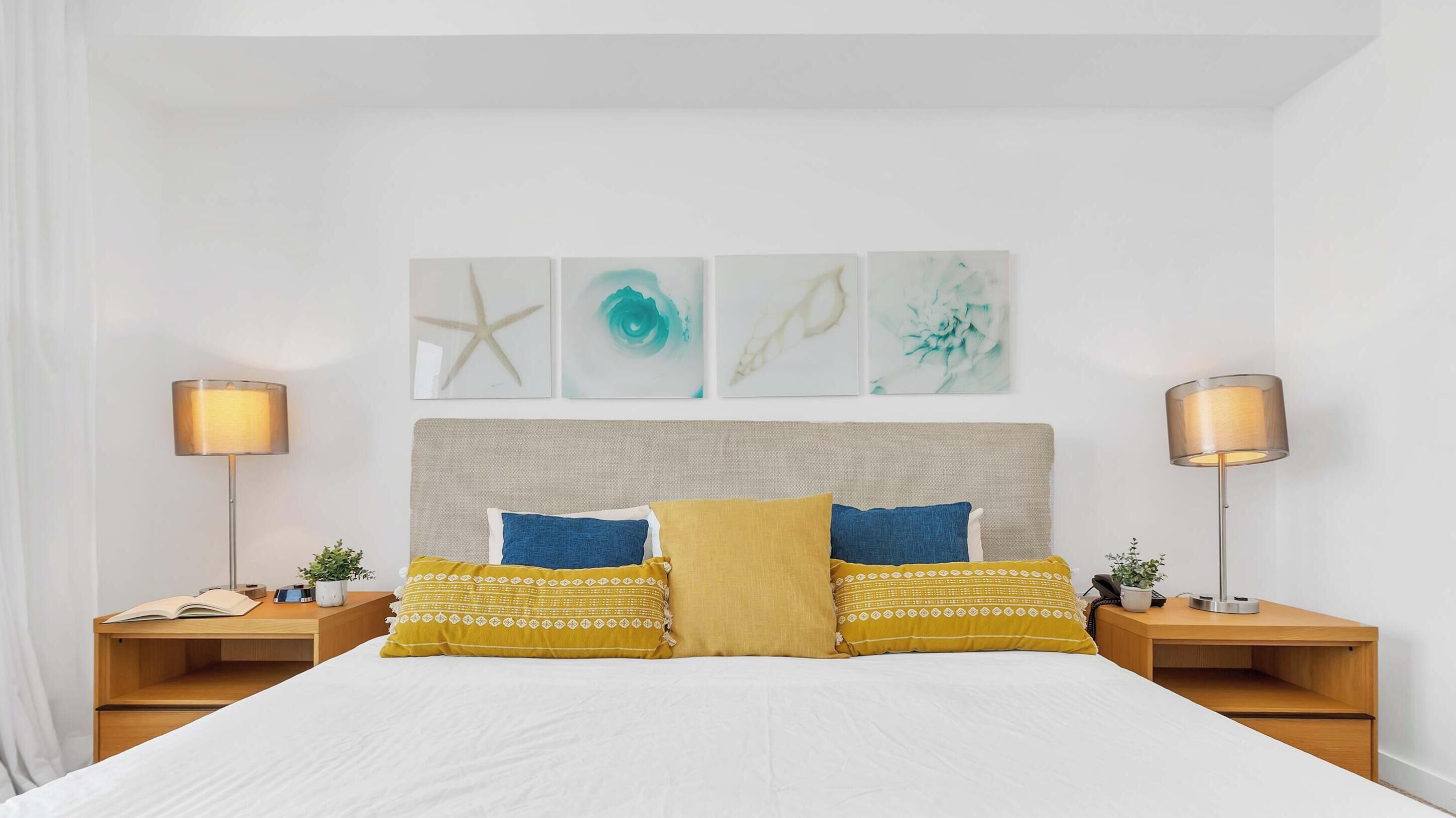A hotel room with a large bed, two bedside tables, and a headboard with wall art.