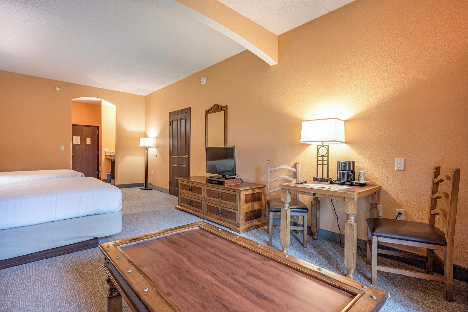 Habitación de hotel con cama, escritorio con lámpara, televisión, cómoda y una mesita.