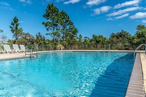 Una piscina con agua cristalina azul, rodeada de árboles y un cielo despejado.