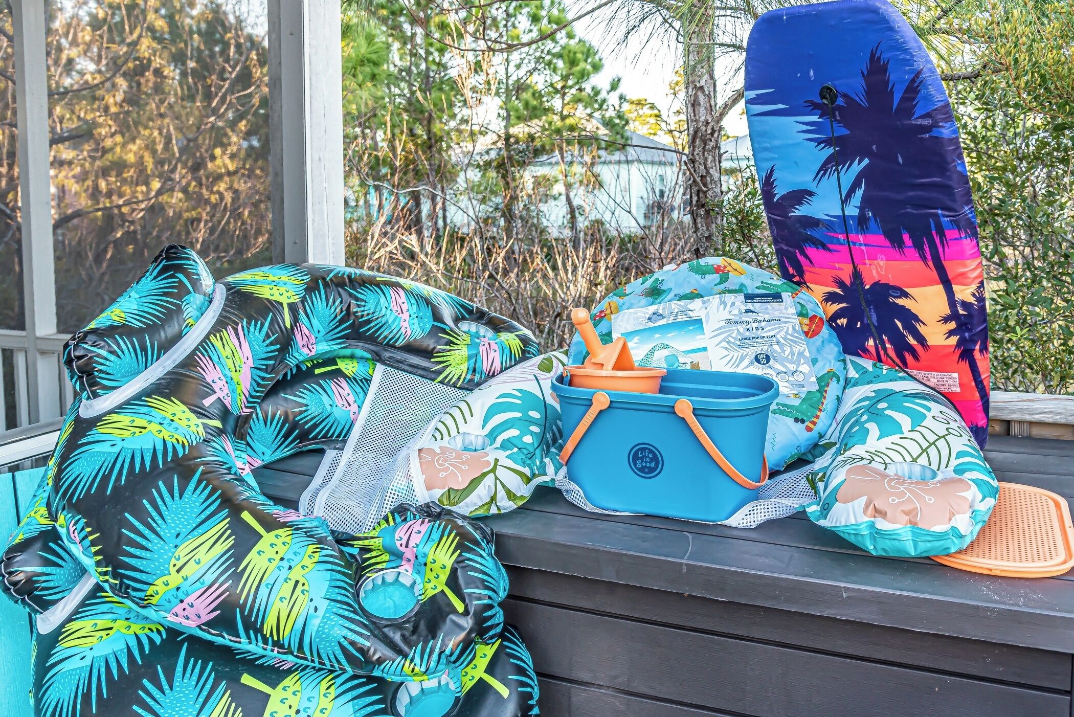 Uma coleção de objetos coloridos com tema praiano, incluindo um maiô, uma bolsa de praia e um travesseiro, dispostos em um banco de madeira.