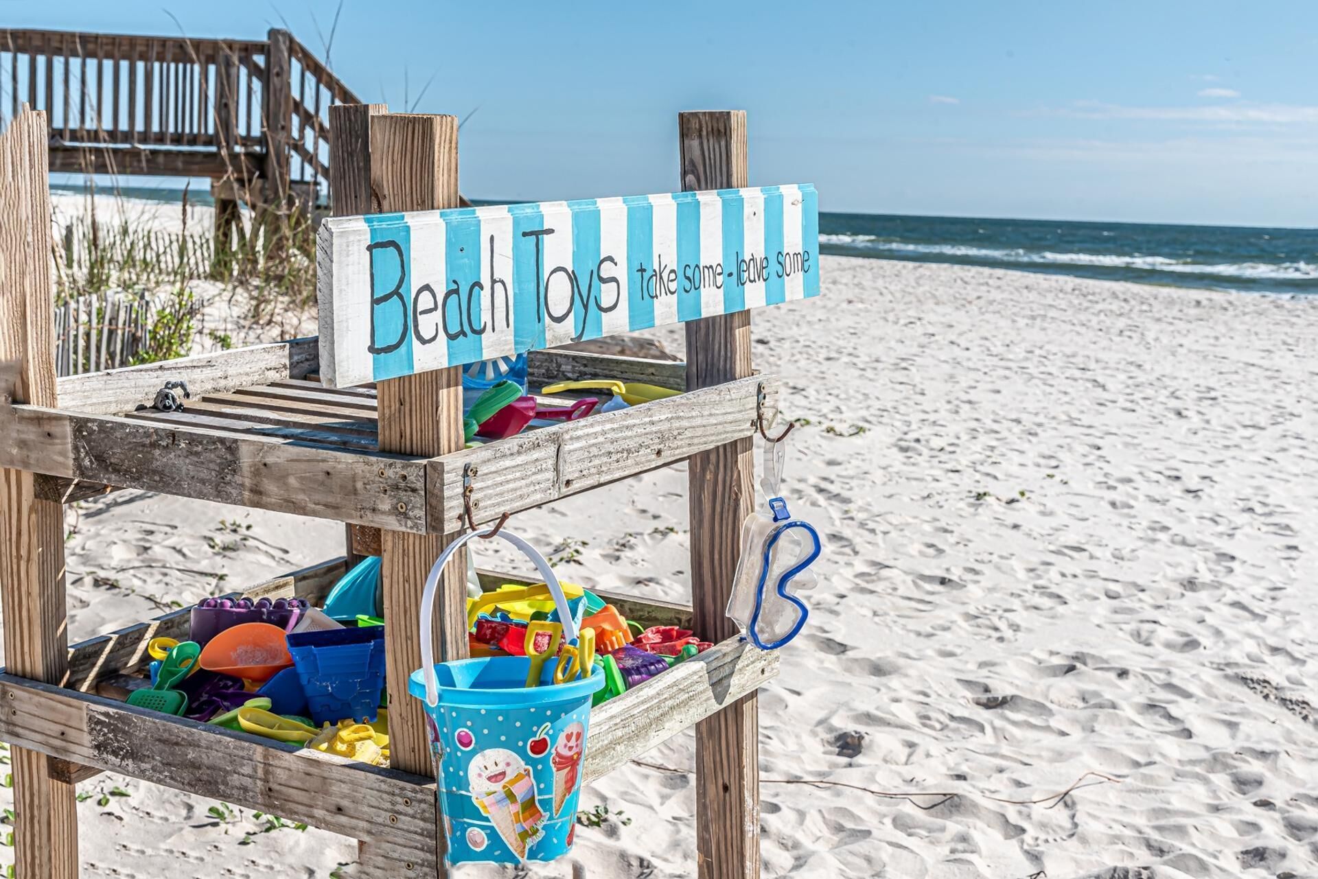 Ein Verleihstand für Strandspielzeug mit einem Schild, auf dem steht: 'Strandspielzeug nehmen – etwas zurücklassen.'