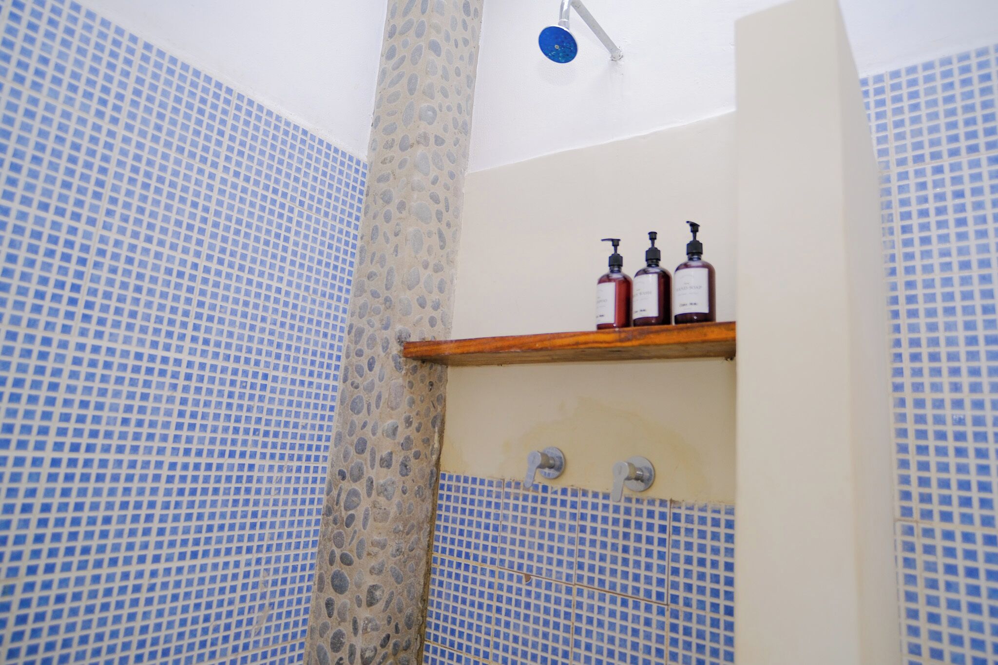 A bathroom with a shower, tiled walls, and a shelf with bottles.