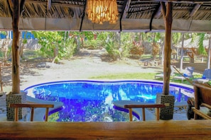 A pool area with a thatched roof, lounge chairs, and a view of the surrounding greenery. - Las Golondrinas KM-59 (Chiltiupan)