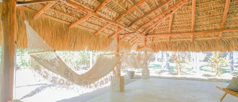 Una construcción con techo de paja, una hamaca y suelo de hormigón.