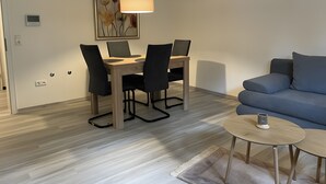 A modern living room with a dining area, a blue sofa, a round coffee table, and a pendant light.
