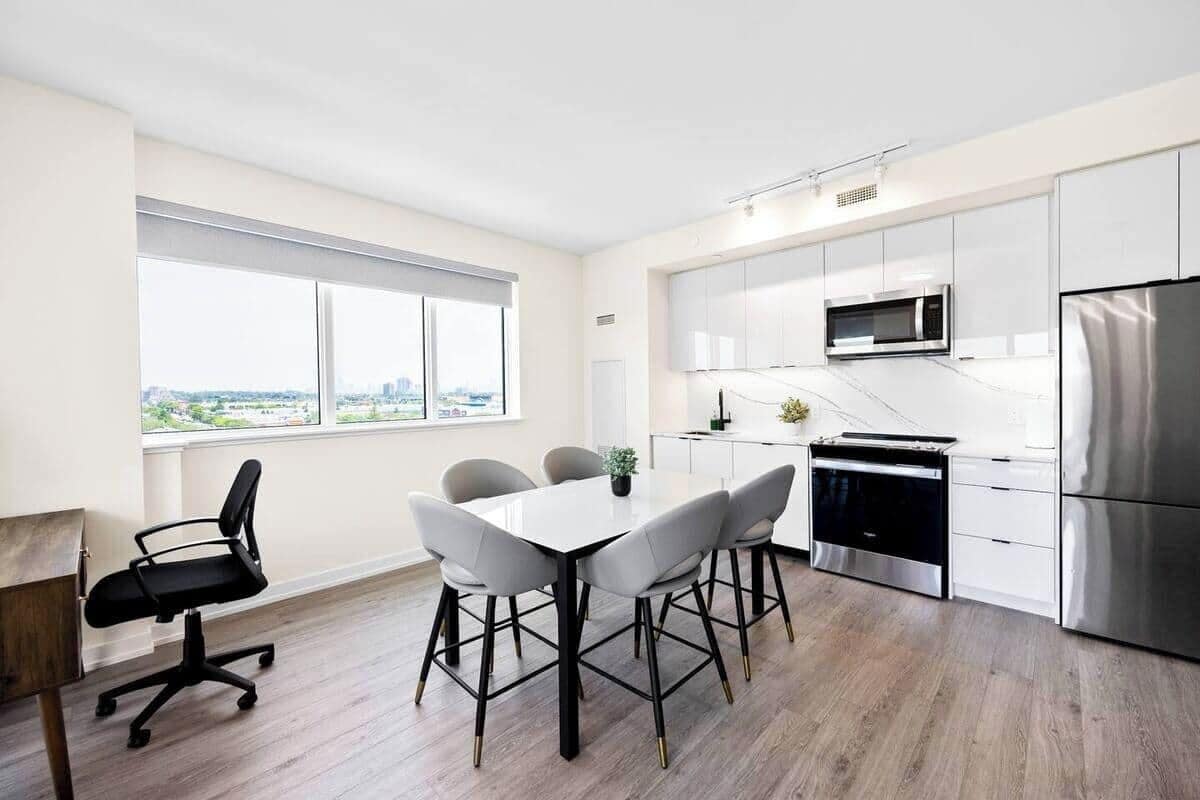 Una cocina moderna con armarios blancos, electrodomésticos de acero inoxidable y una zona de comedor con una mesa y sillas blancas.