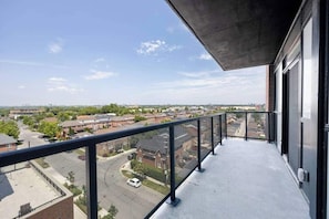 Ein Balkon mit Blick auf ein Wohngebiet, einen klaren Himmel und einen Parkplatz.