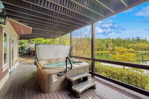 A hot tub on a wooden deck with a view of a lake and trees. - 3BR waterfront home with dock and hot tub (Bainbridge Island)