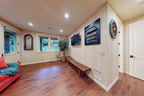 A room with wooden flooring, a bench, a television, and a door. - 3BR waterfront home with dock and hot tub (Bainbridge Island)