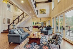A spacious living area with a wooden staircase, a dining area, and large windows offering a view of the outdoors. - 3BR waterfront home with dock and hot tub (Bainbridge Island)
