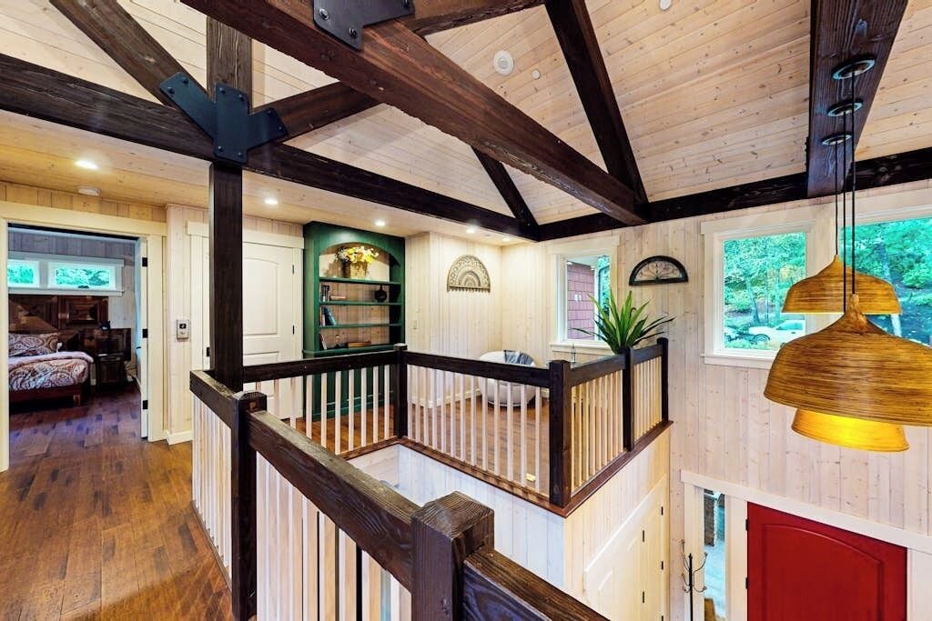 A multi-level wooden interior with a staircase, a red door, and a hanging lamp.