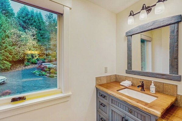 A bathroom with a large window, a wooden vanity, a mirror, and a sink. - 3BR waterfront home with dock and hot tub (Bainbridge Island)