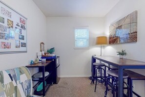 Een compacte kamer met kitchenette, een klein eethoekje en een wand versierd met ingelijste foto's.