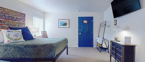 A bedroom with a bed, a desk, a TV, and a door.