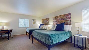A bedroom with two beds, a desk, and a window.