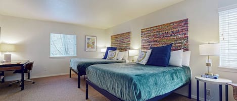 A bedroom with two beds, a desk, and a window.