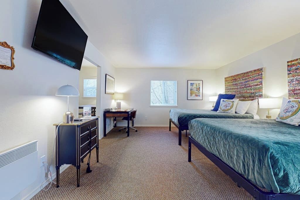 A hotel room with two beds, a desk, a chair, a TV mounted on the wall, and a window.
