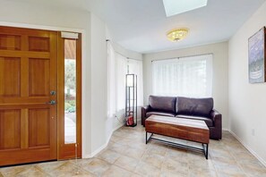 A room with a wooden door, a brown leather sofa, a coffee table, and a ceiling light fixture. - Fantastic 3BR Oceanview with decks, gas grill (Sequim)