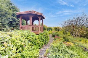 A garden with a wooden gazebo, a gravel path, and various plants. - Fantastic 3BR Oceanview with decks, gas grill (Sequim)