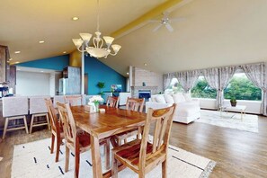 A spacious living area with a wooden dining table, white sofa, and a view of greenery through large windows. - Fantastic 3BR Oceanview with decks, gas grill (Sequim)