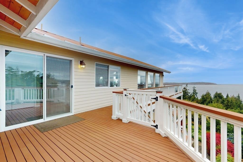 A wooden deck with a white railing, a sliding glass door, and a view of the ocean.
