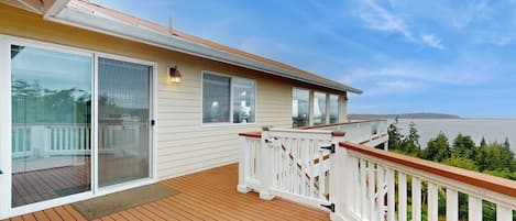 A wooden deck with a white railing, a sliding glass door, and a view of the ocean.