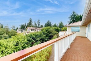 A wooden deck with a white railing overlooking a lush green landscape and residential buildings. - Fantastic 3BR Oceanview with decks, gas grill (Sequim)